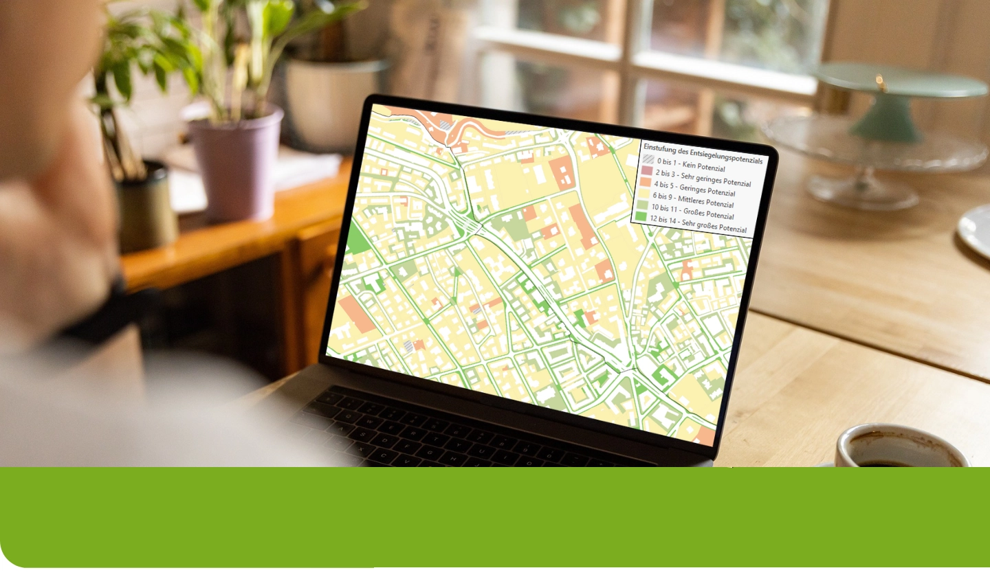 Person betrachtet am Laptop eine farblich abgestufte Karte zur Einstufung des Entsiegelungspotenzials – grün markierte Flächen mit hohem Potenzial, orange und rot mit geringem Potenzial. Symbolbild für digitale Kartenanalyse bei onmaps.