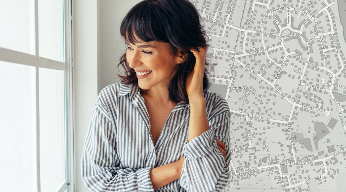 Lächelnde Architektin oder Stadtplanerin steht vor einem Fenster, im Hintergrund ein detaillierter Stadtplan